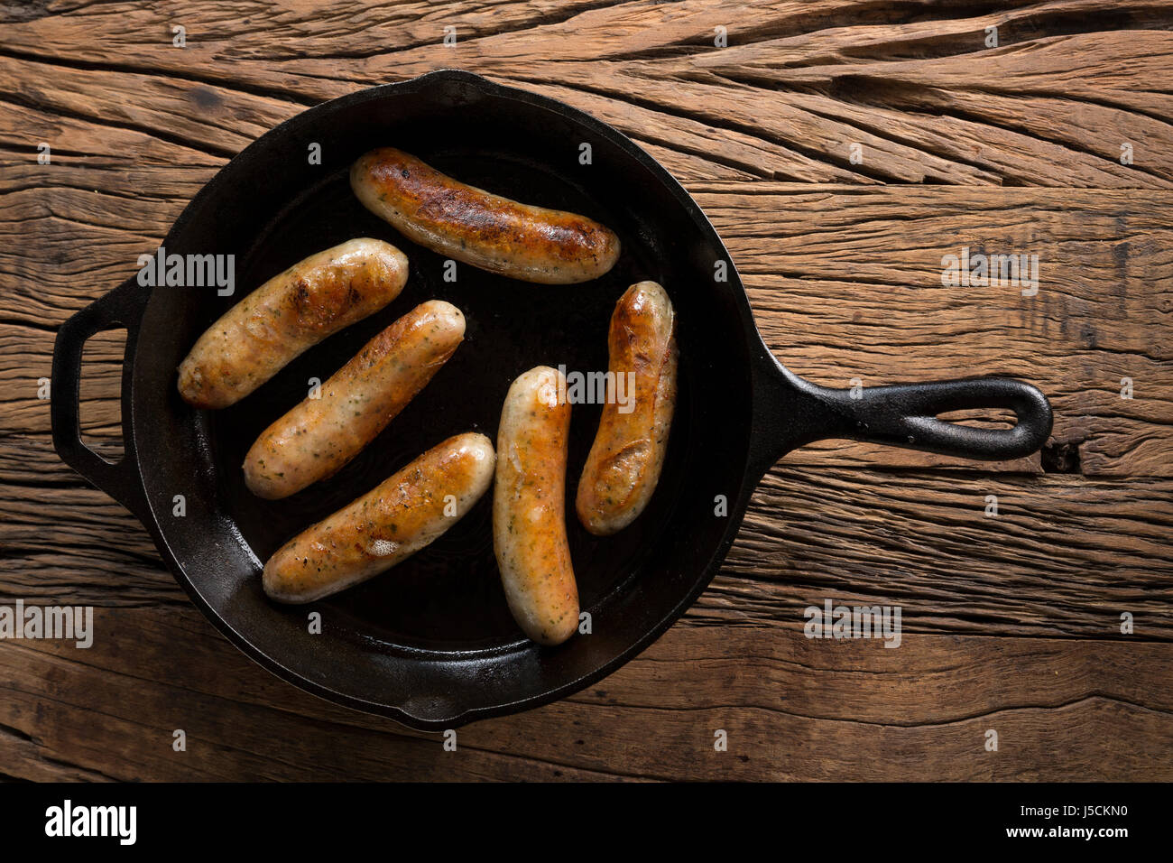 Gourmet butchers sausages in a frying pan, on a rustic wooden background. Stock Photo