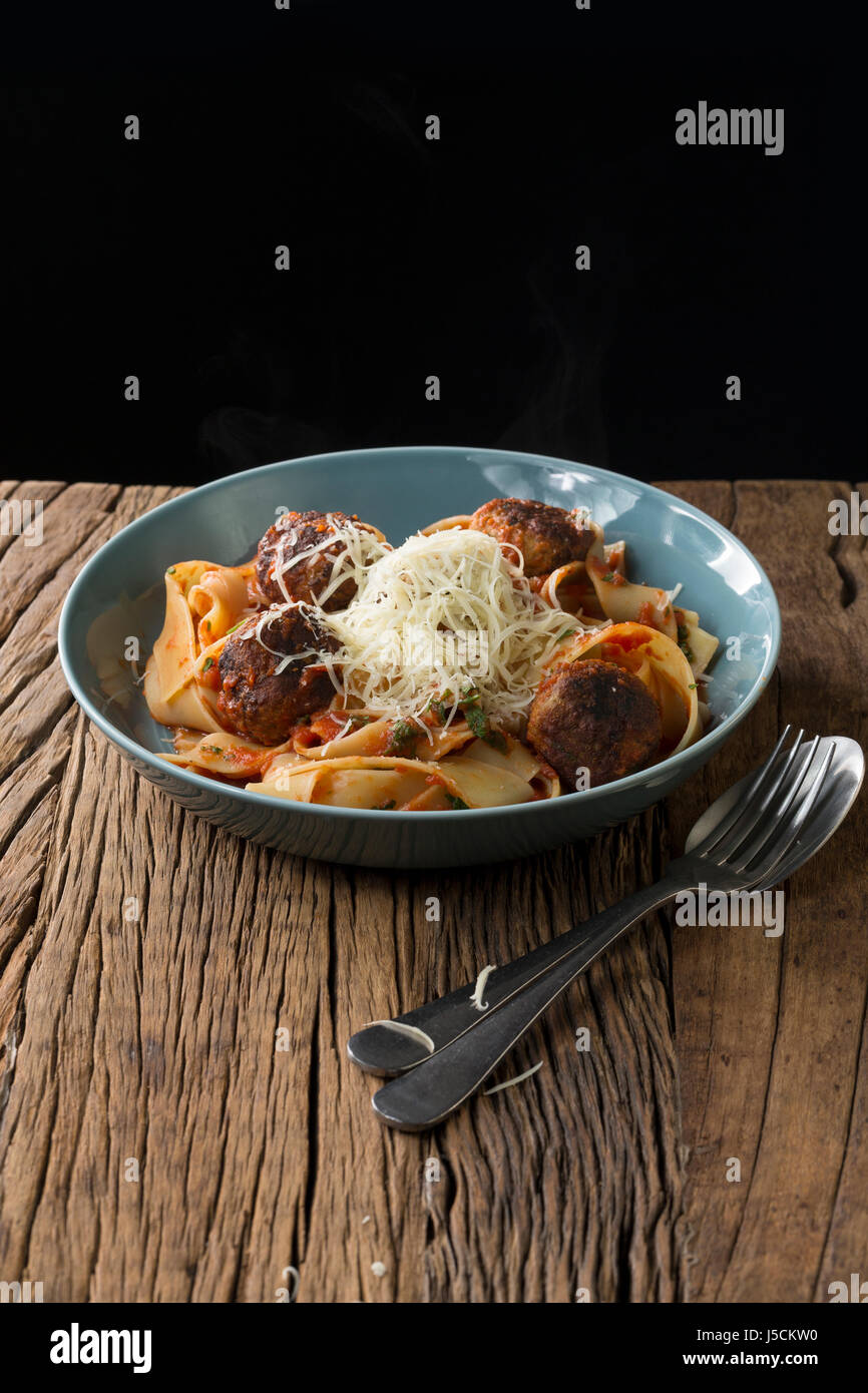 Italian meat balls with pasta, tomato sauce and Parmesan cheese. Sitting on a rustic wooden table. Stock Photo