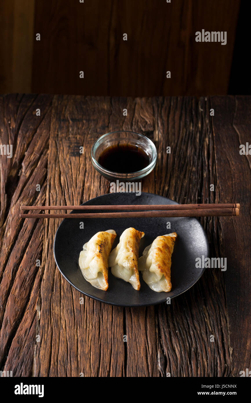 A plate of Japanese gyoza dumplings sitting on a rustic wooden table. Stock Photo