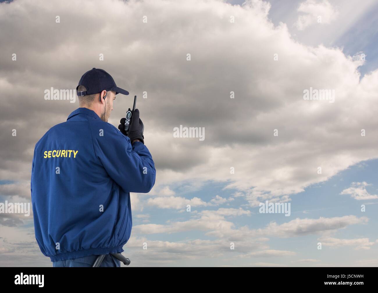 Digital composite of Rear view of security guard using radio against cloudy sky Stock Photo