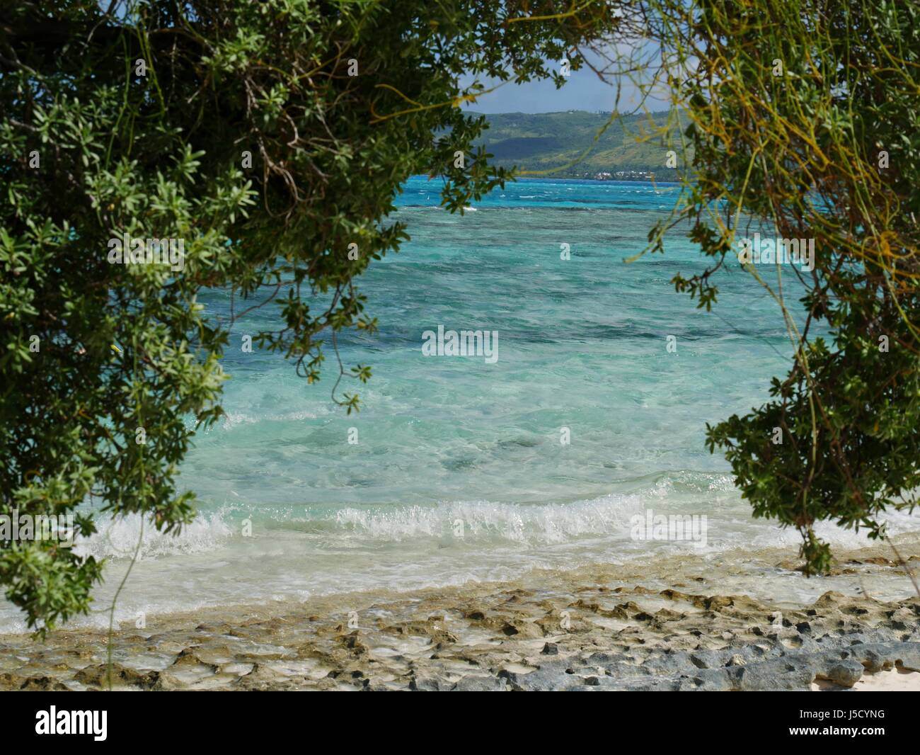The rocky shoreline and clear blue waters at the backside of Managaha Island,  curtained by thick foliage. Stock Photo