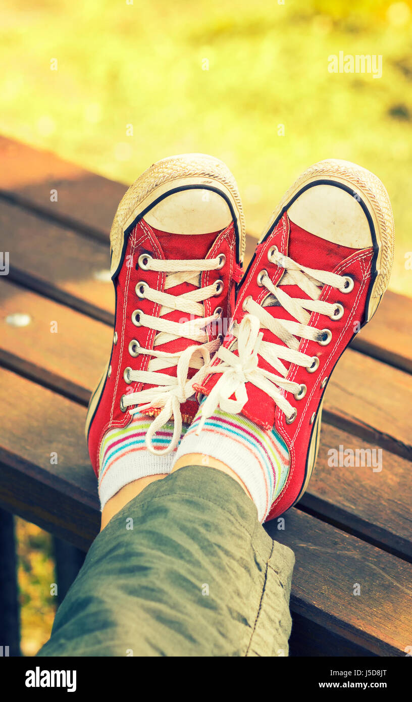 Woman's feet in a red canvas sneakers sitting on a bench Stock Photo