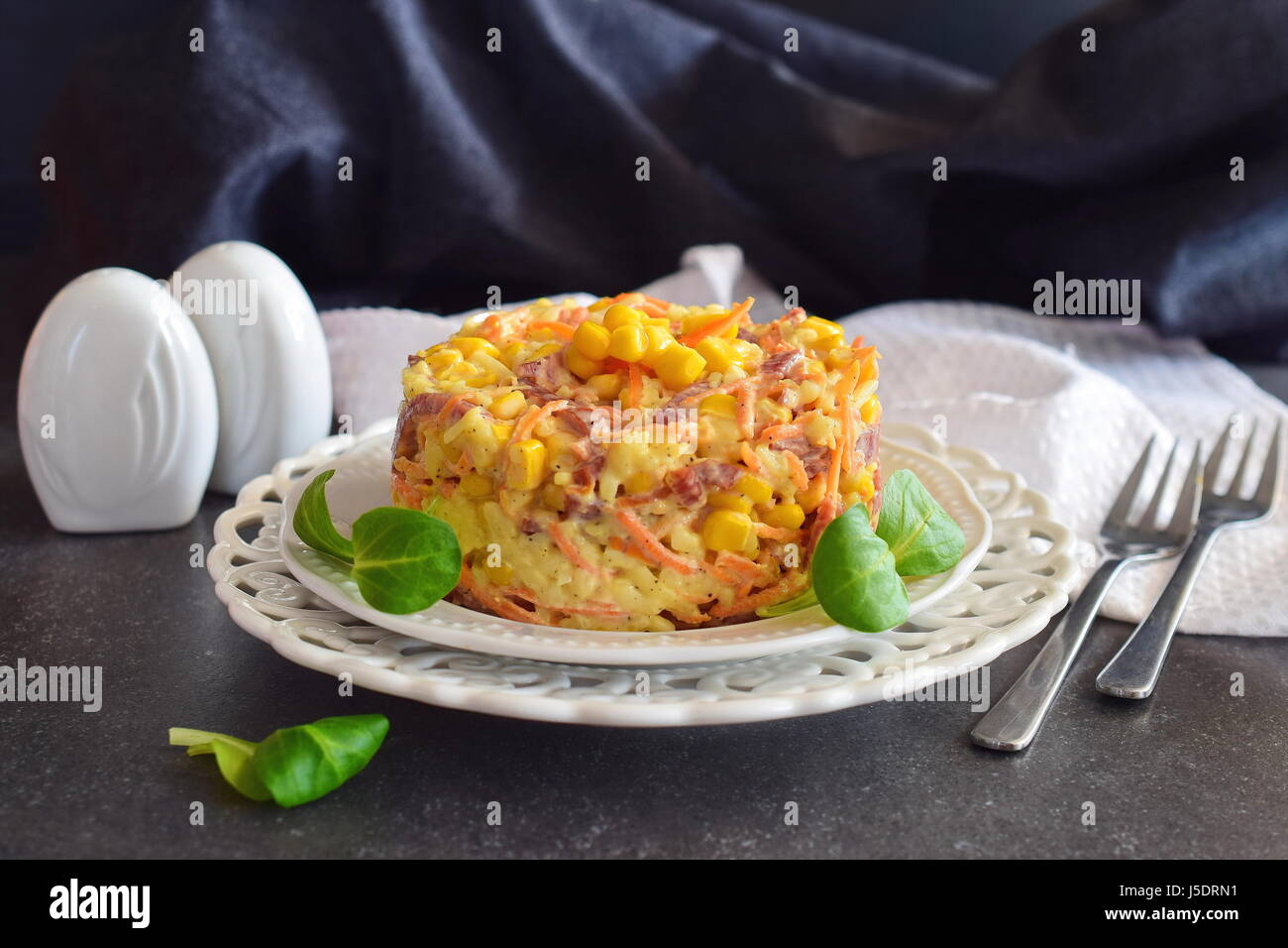 Salad with smoked sausage, corn, cheese, fresh carrot, egg, garlic and yogurt on a white plate on a abstract background. Stock Photo