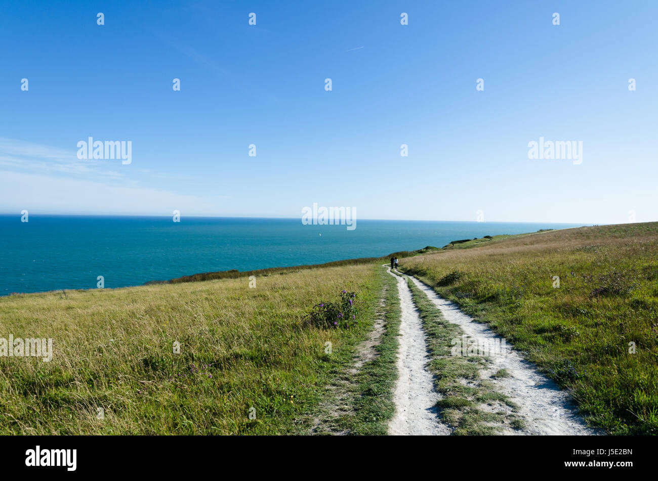 A footpath towards the sea with a couple walking in the distance Stock Photo