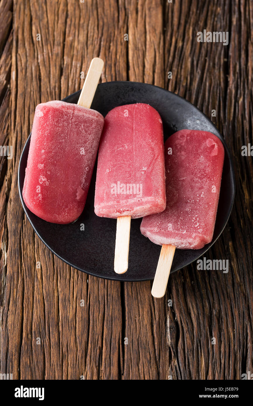 Three Homemade Raspberry and vanilla ice pops on a rustic wood background. 3 Berry icecream popsicle. Summer food. Stock Photo