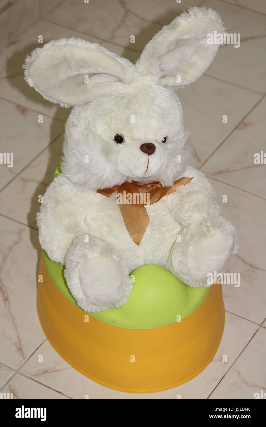 White teddy bunny toy sitting on a kids toilet Stock Photo