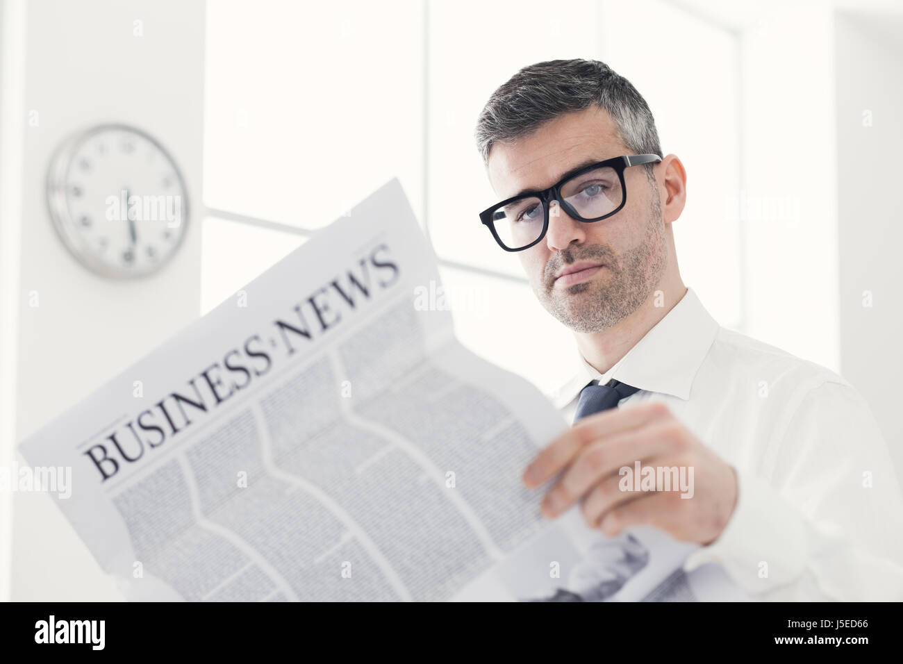 Confident businessman with glasses reading a financial newspaper in his ...