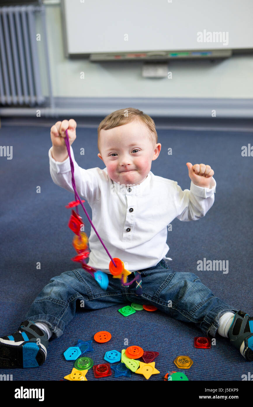 down Syndrome boy at nursery. He is making a toy necklace which he is holding up to the camera proudly. Stock Photo
