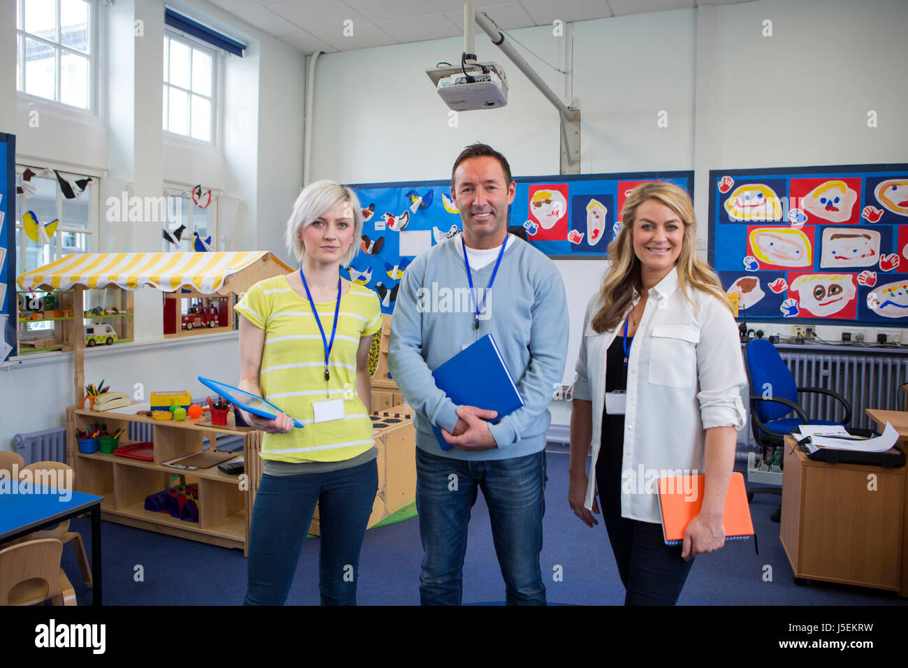 Three teachers standing in the classroom of a school building. They are holding school work and smiling at the camera. Stock Photo