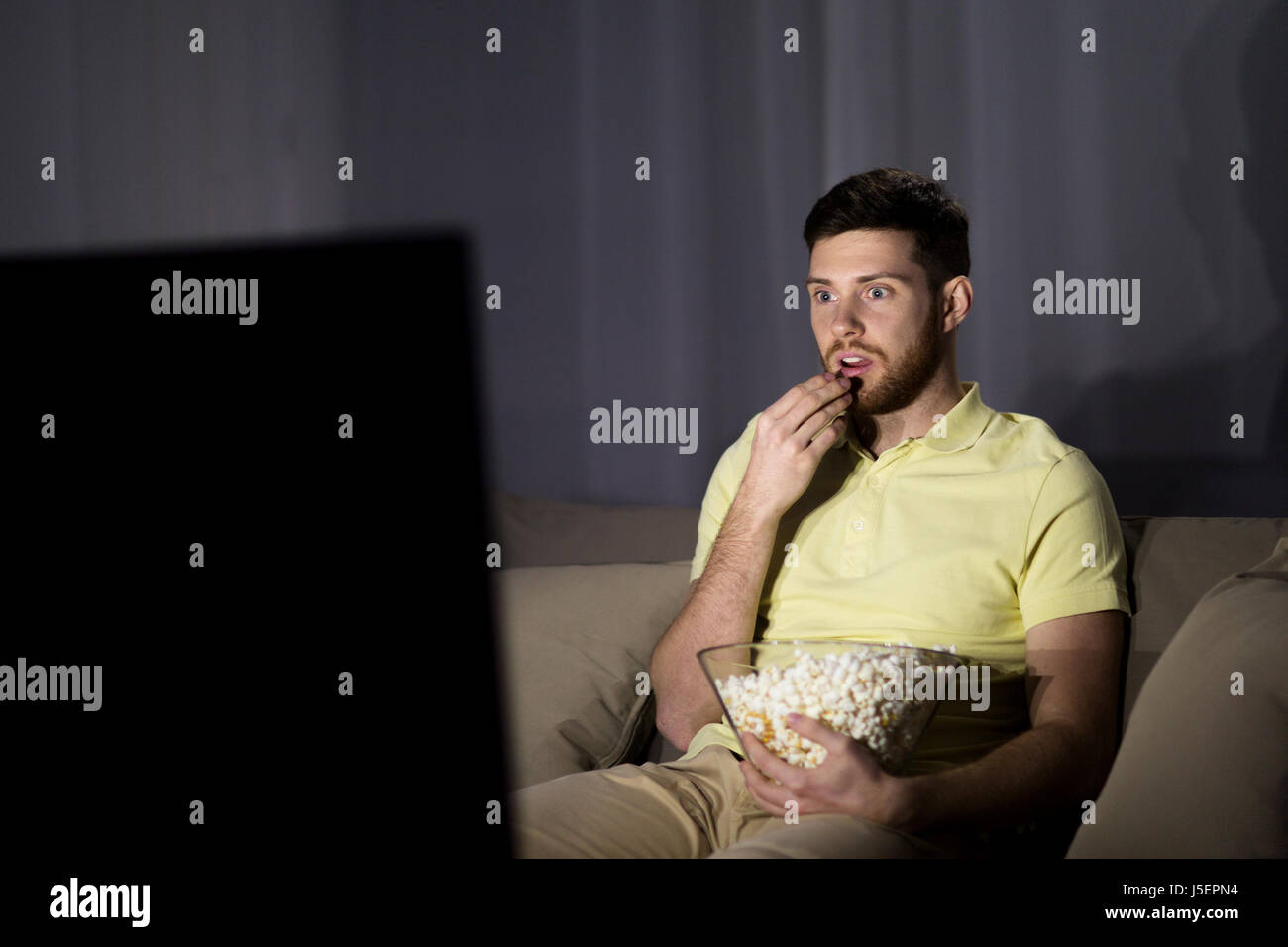 man watching tv and eating popcorn at night Stock Photo Alamy