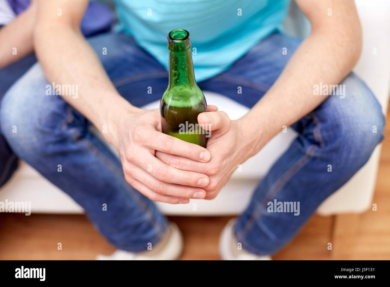 men with beer bottles sitting on sofa at home Stock Photo
