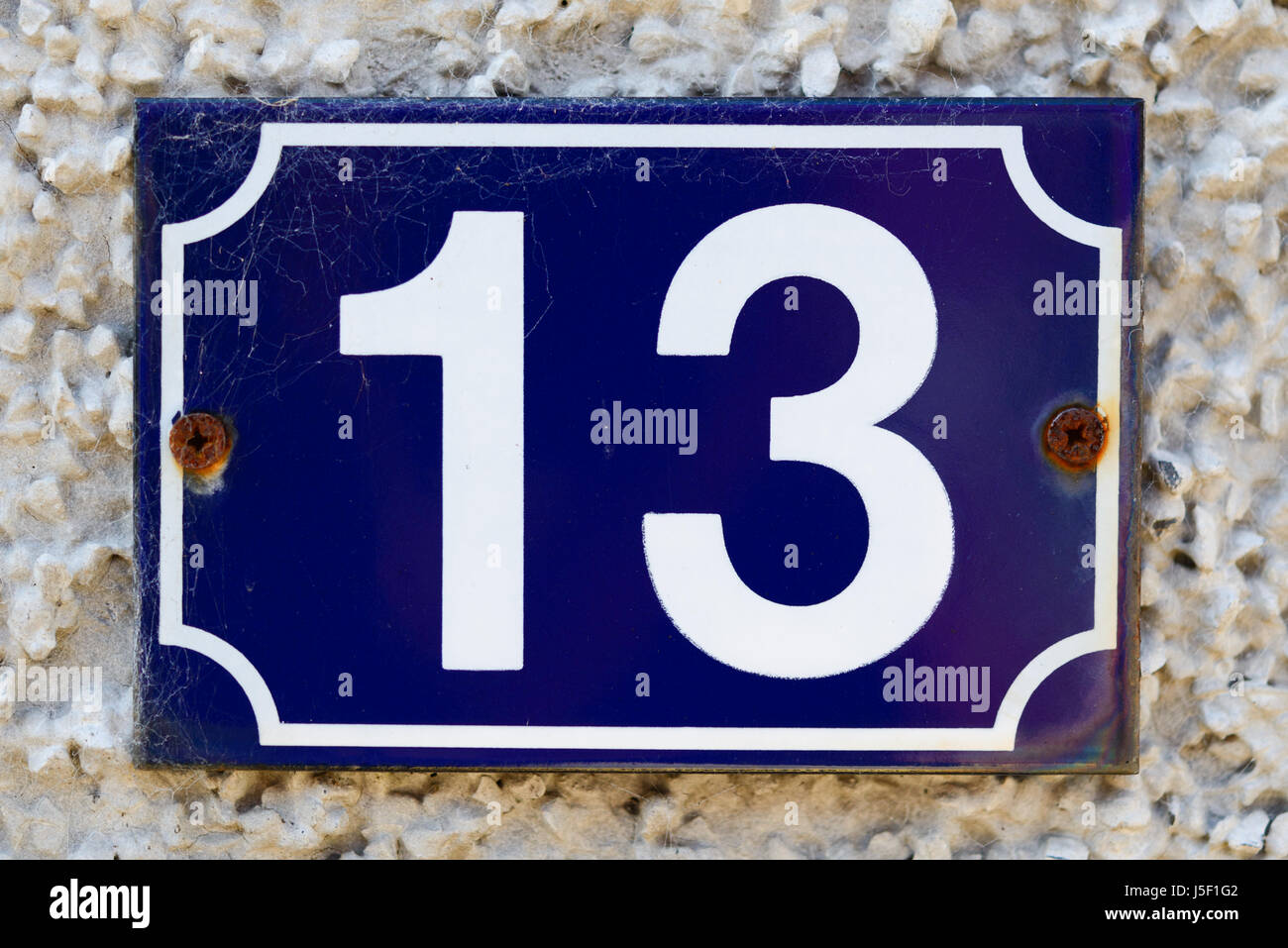 House number 13ca in white on a dark blue background, fastened to a pebble-dashed wall. Stock Photo