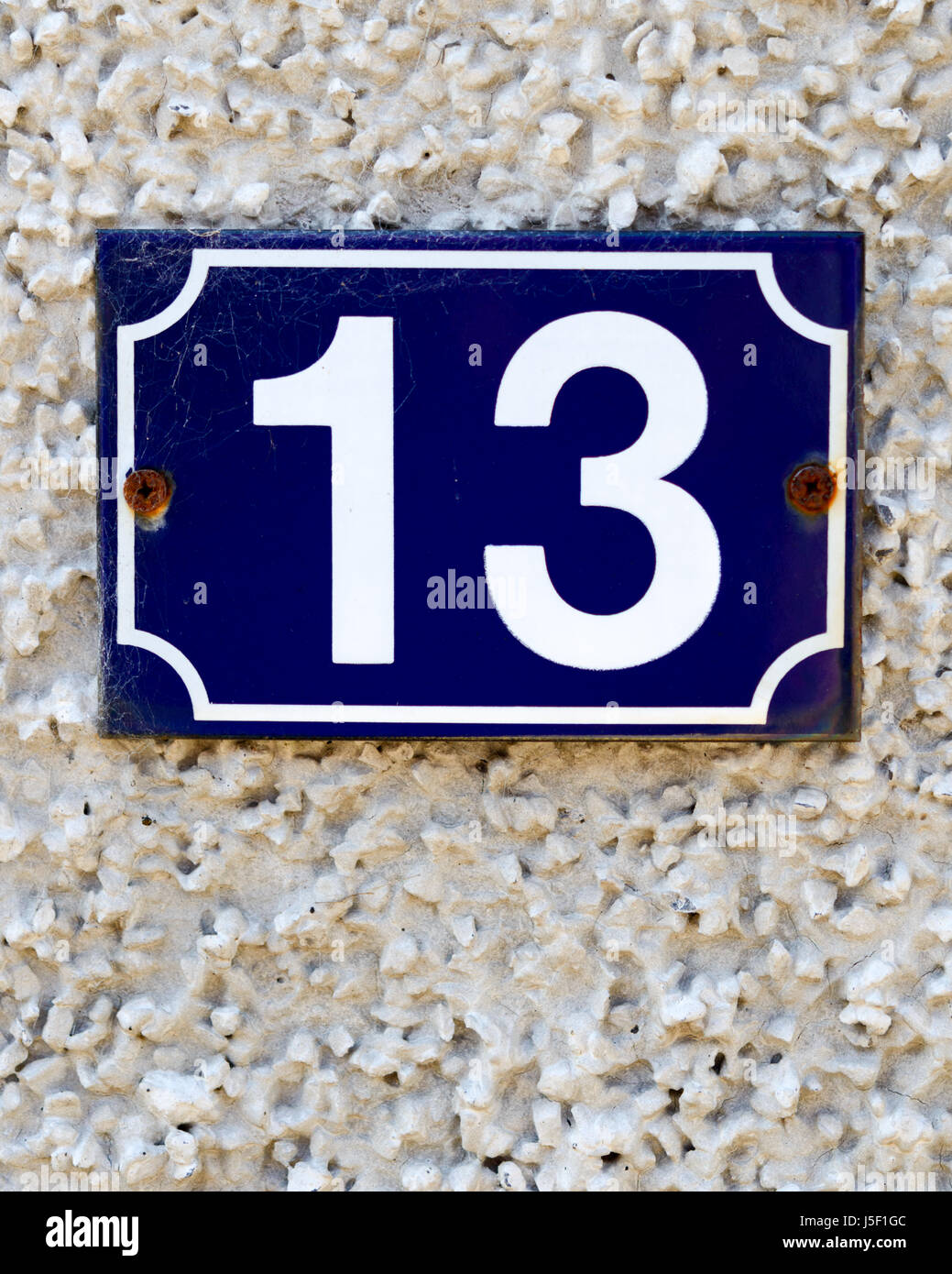 House number 13ca in white on a dark blue background, fastened to a pebble-dashed wall. Stock Photo