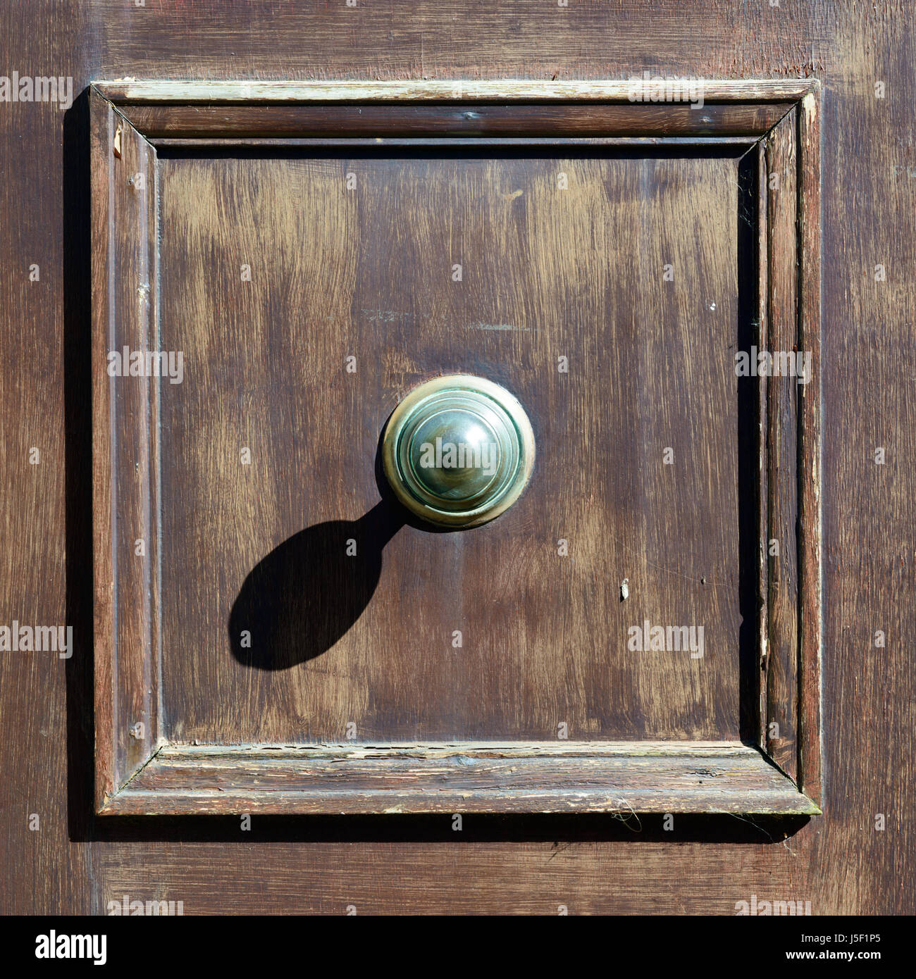 Large door knob casting a strong shadow on a faded door. Stock Photo