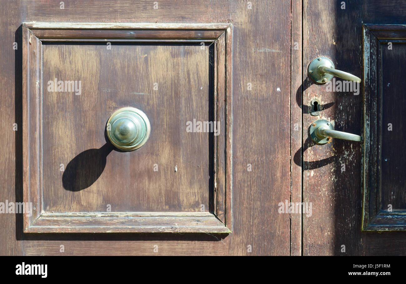 Large door knob casting a strong shadow on a faded door and featuring two separate door handles. Stock Photo
