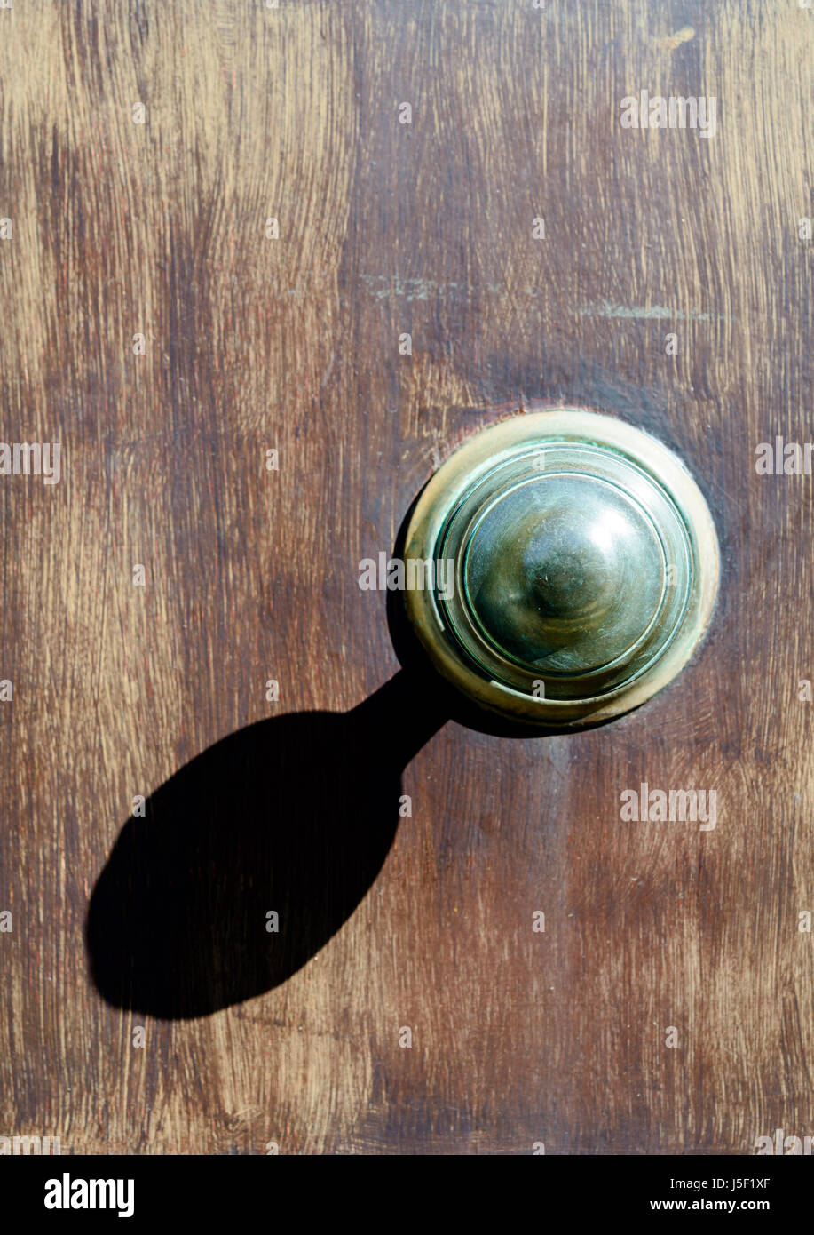 Large door knob casting a strong shadow on a faded door. Stock Photo