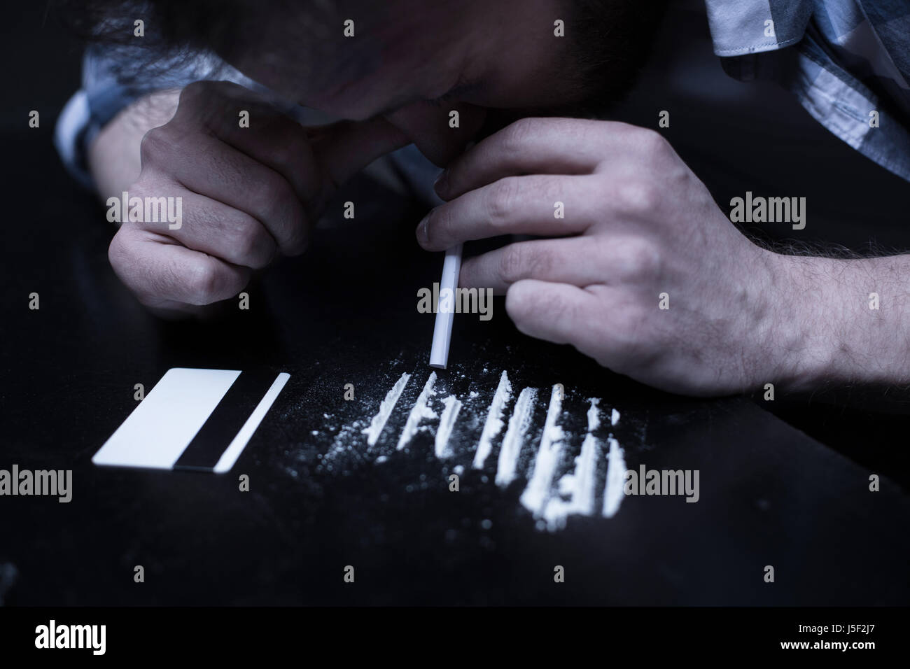 Involved drug addict inhaling cocaine lines in the dark place Stock Photo