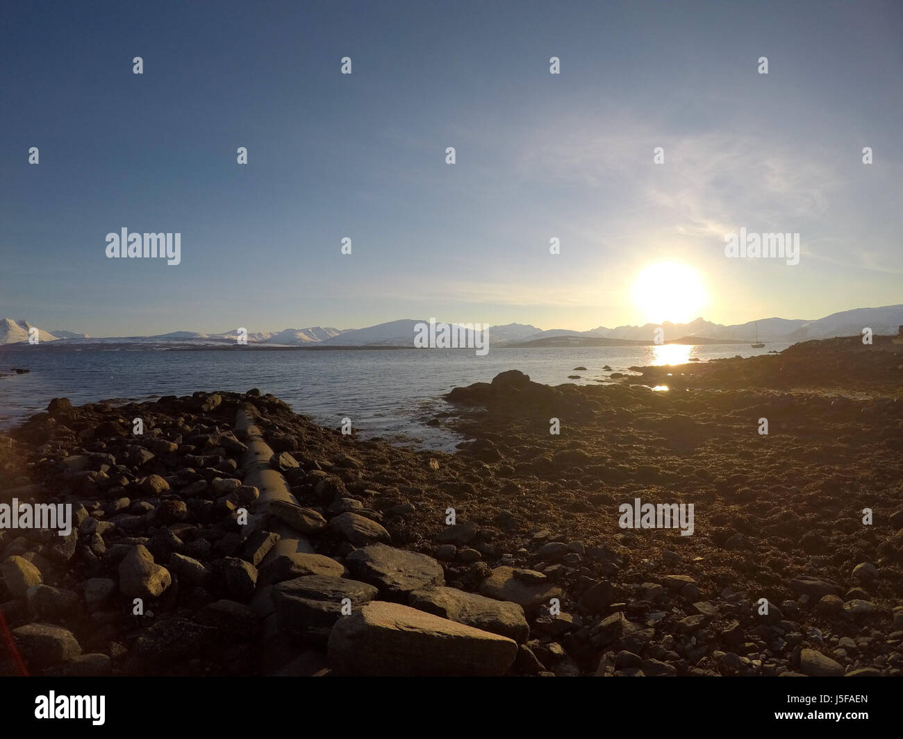 sunset over snowy mountain and rocky seashore Stock Photo - Alamy