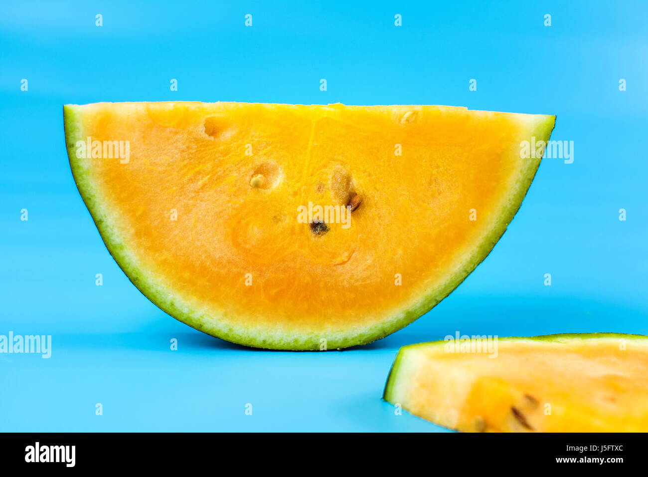 Yellow watermelon fruit slice against blue background Stock Photo - Alamy