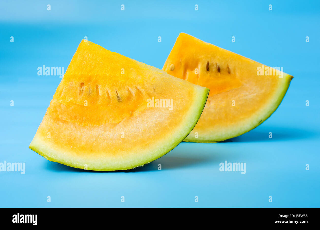 Yellow watermelon fruit slice against blue background Stock Photo - Alamy