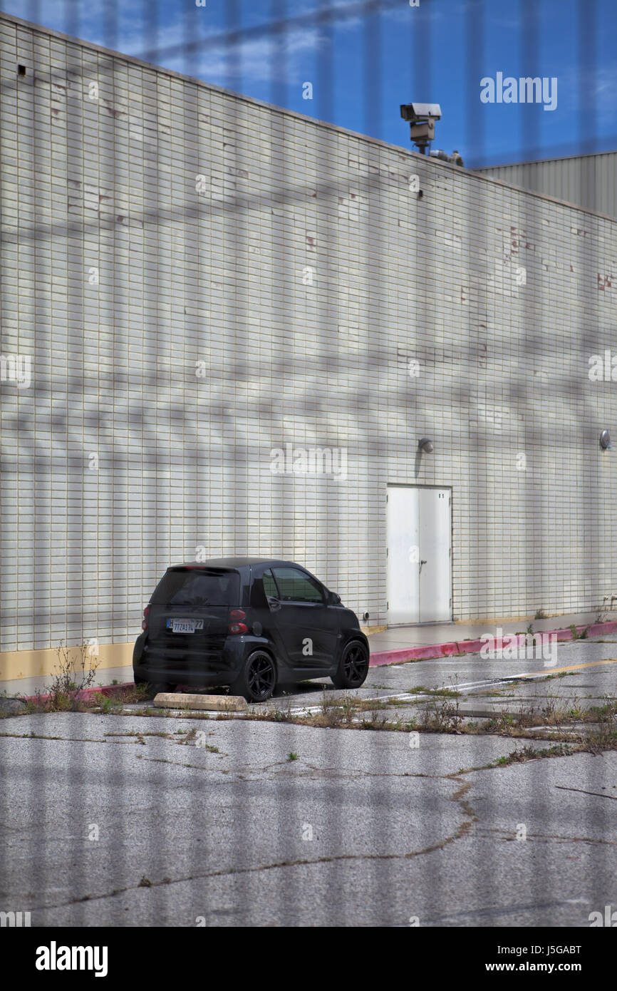 Black Smart Car parked by white brick building with surveillance camera Stock Photo
