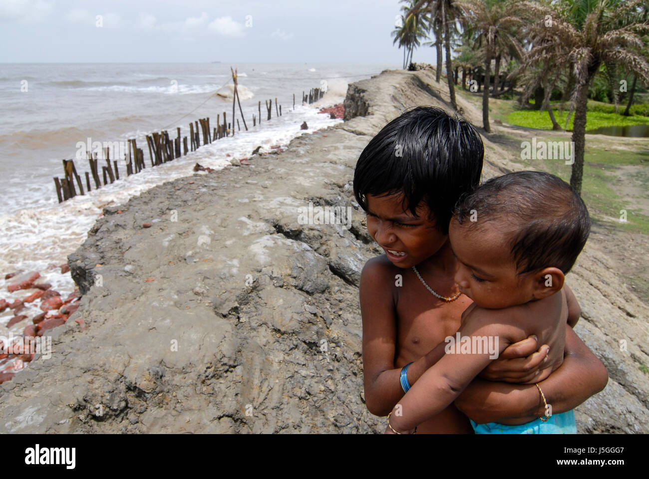 INDIA, West Bengal, Ganges river delta Sundarbans , Sagar Island , broken dyke due to sea erosion and rising sea levels, girl carry infant Stock Photo