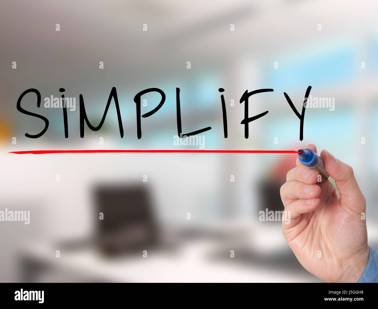 Businessman hand writing Simplify with marker on transparent wipe board isolated on office. Stock Image Stock Photo