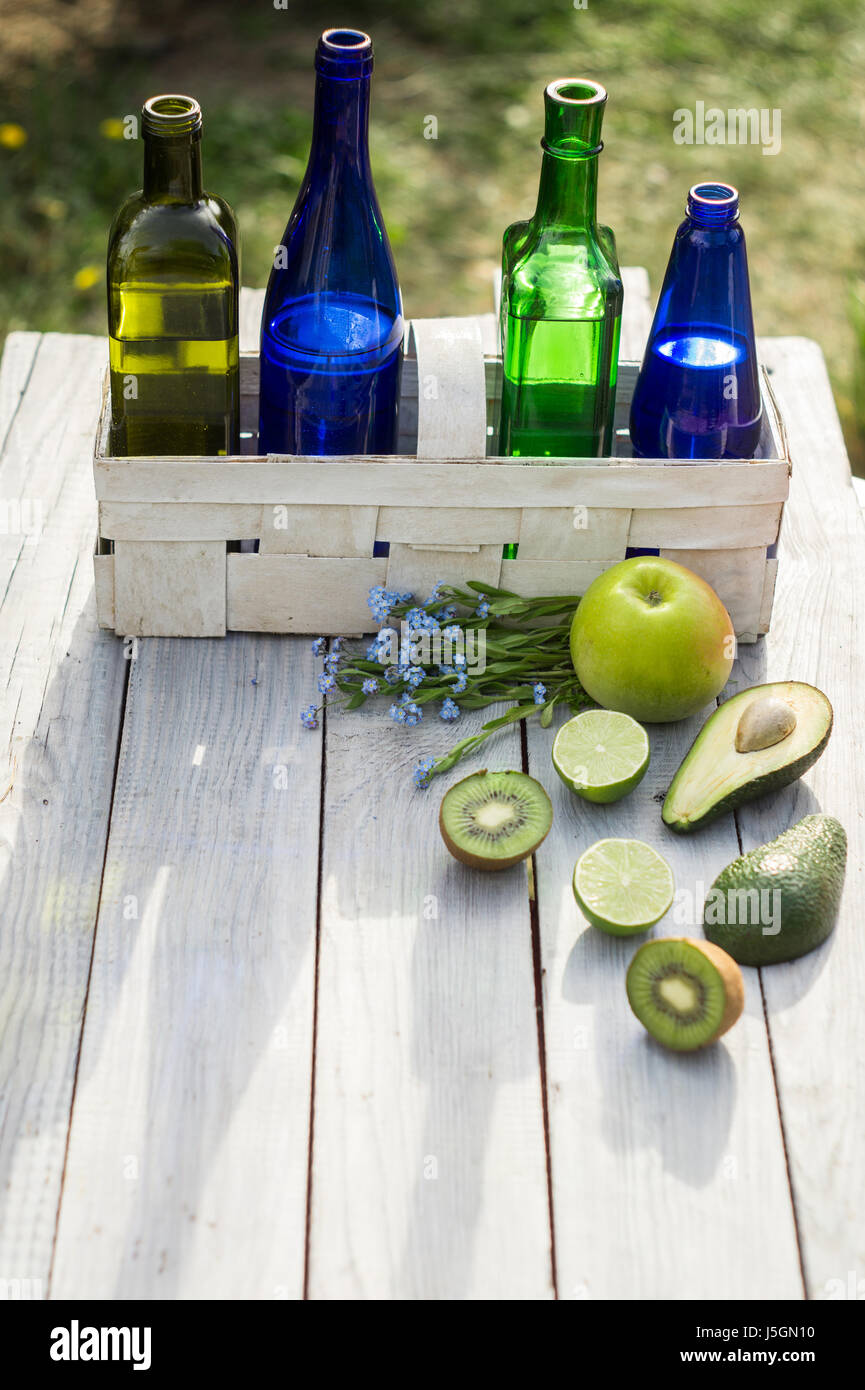 Four bottles of drinks in a white basket and fruits on a white table Stock Photo