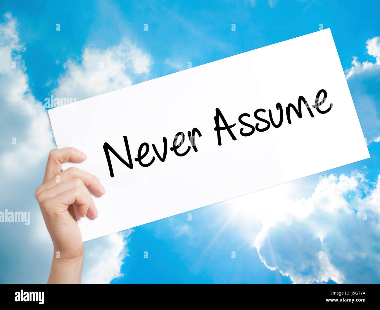 Never Assume Sign on white paper. Man Hand Holding Paper with text. Isolated on sky background.  Business concept. Stock Photo Stock Photo