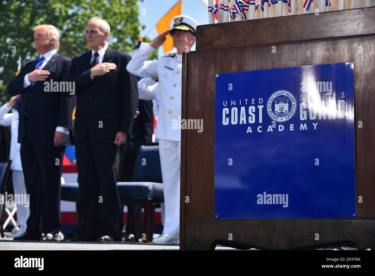 New London, USA. 17th May, 2017. U.S. President Donald Trump, Homeland Security Secretary John Kelly, center, and Coast Guard Commandant Adm. Paul Zukunft salutes during the national anthem at the 136th Coast Guard Academy commencement ceremony May 17, 2017 in New London, Connecticut. Credit: Planetpix/Alamy Live News Stock Photo