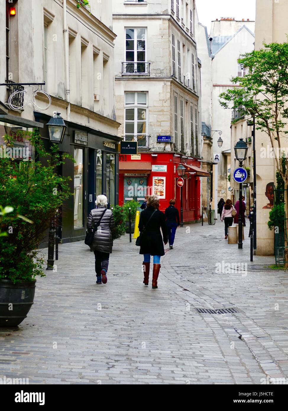 Women in coats/jackets walking away from camera down rue des Rosiers, Paris, France. Stock Photo
