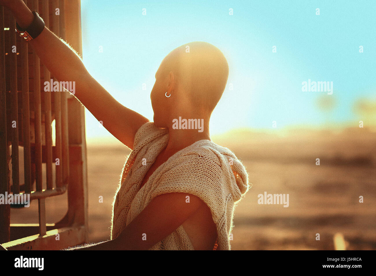 Shaved-headed girl silhouette on the sunset scenery, desert view with blue sky and sands,old vintage trains and railway station backdrop, fasion style Stock Photo
