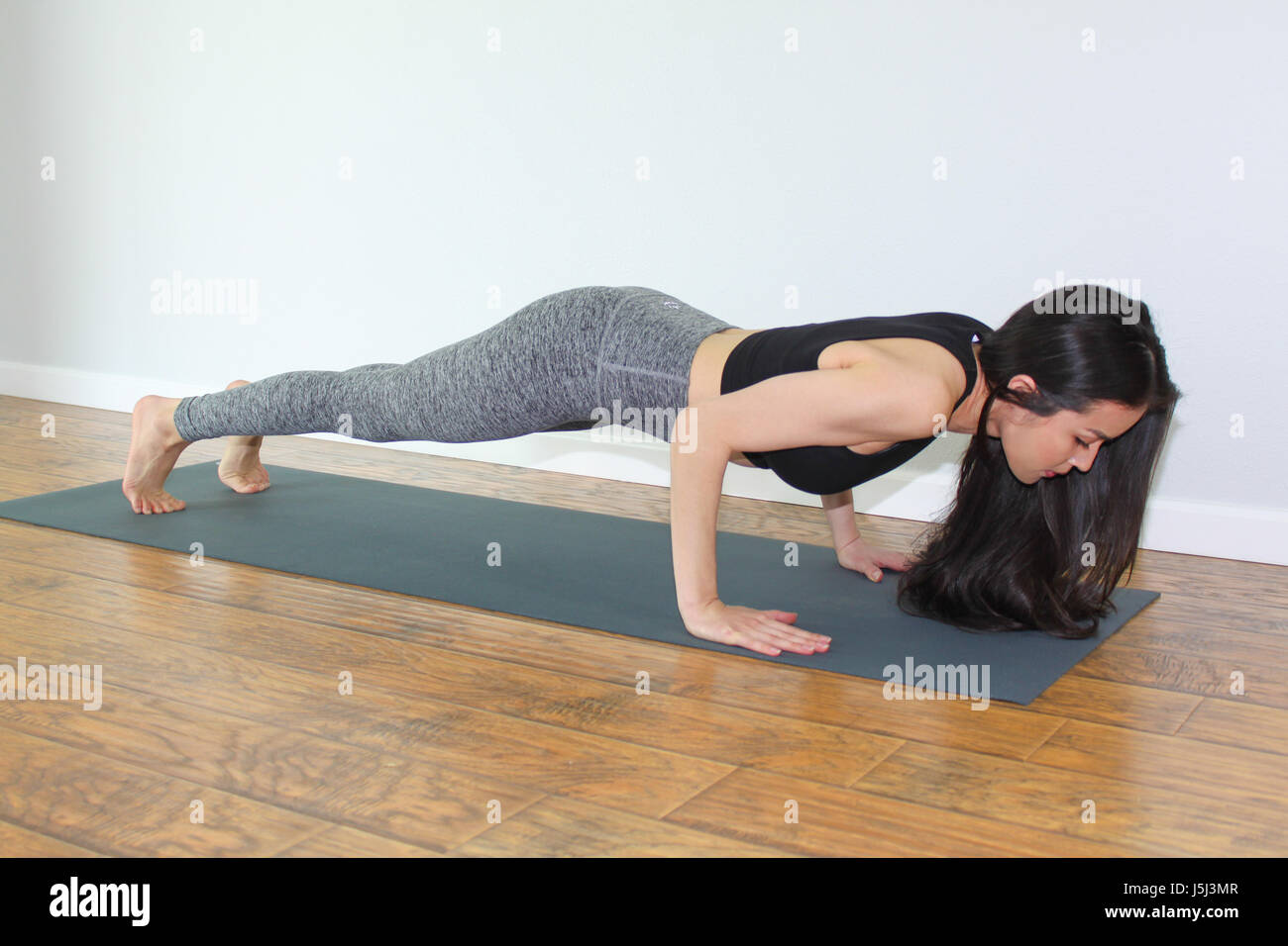 Beautiful woman doing a yoga pose called low plank or chaturanga dandasana. Stock Photo