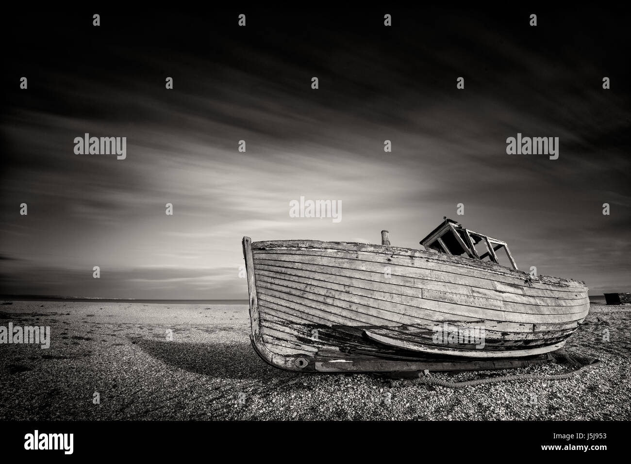 Single abandoned old fishing boat on a pebble beach in monochrome. Dungeness, England Stock Photo