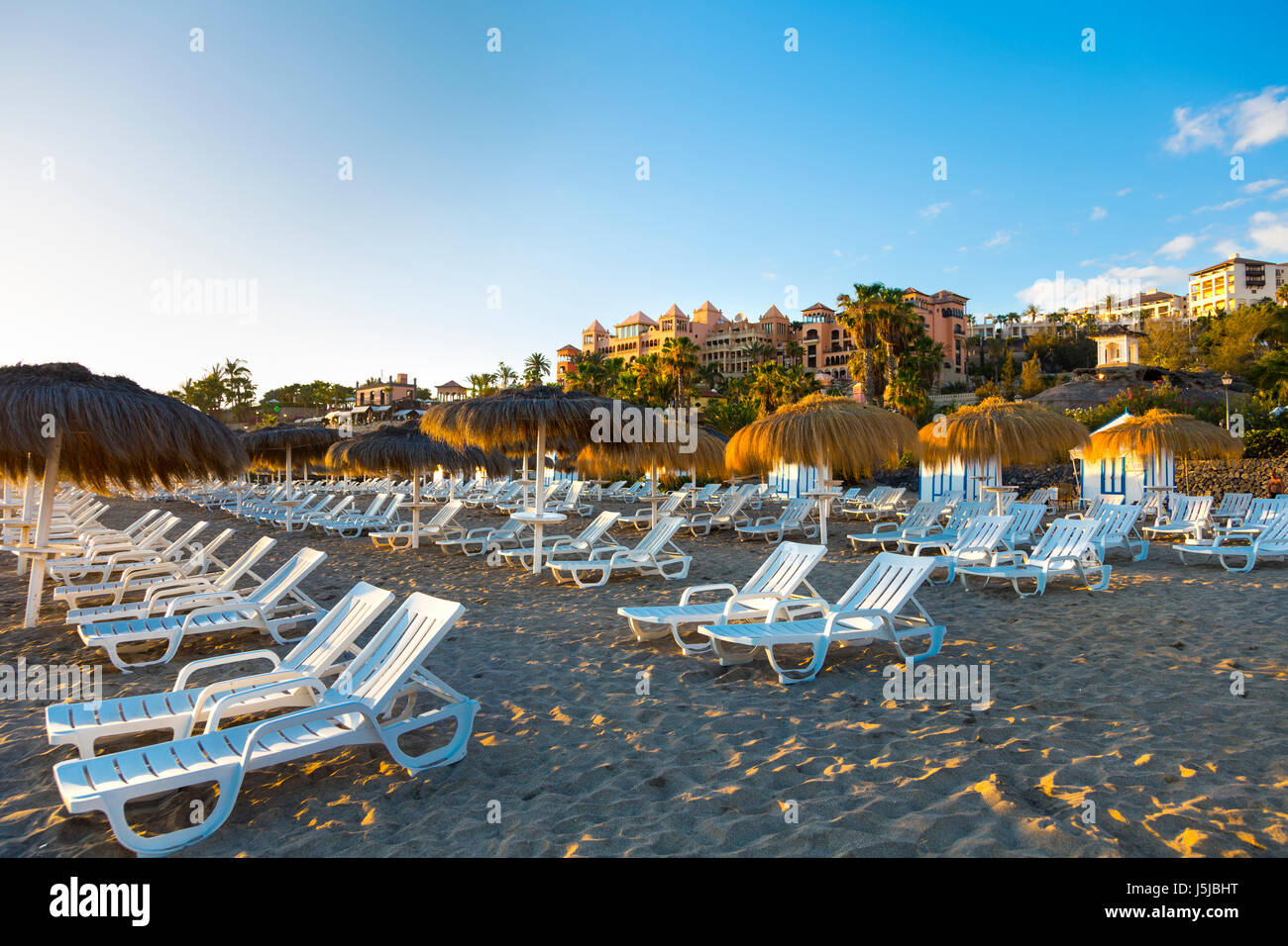 Sun loungers and straw parasols at Playa del Duque beach in Costa Adeje, Tenerife, Spain Stock Photo