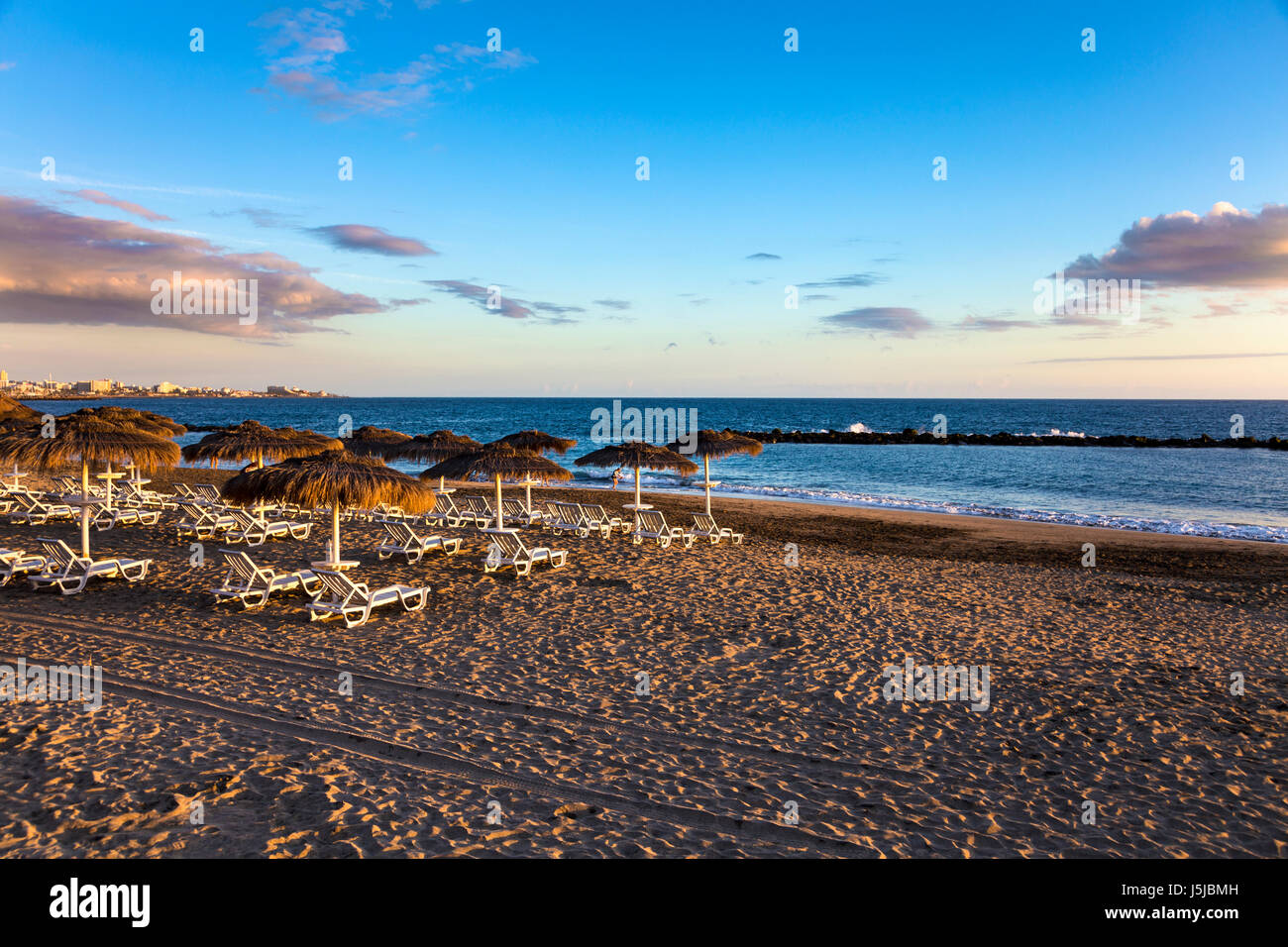 Straw parasols and loungers at sunset on Playa del Duque, Costa Adeje, Tenerife, Spain Stock Photo