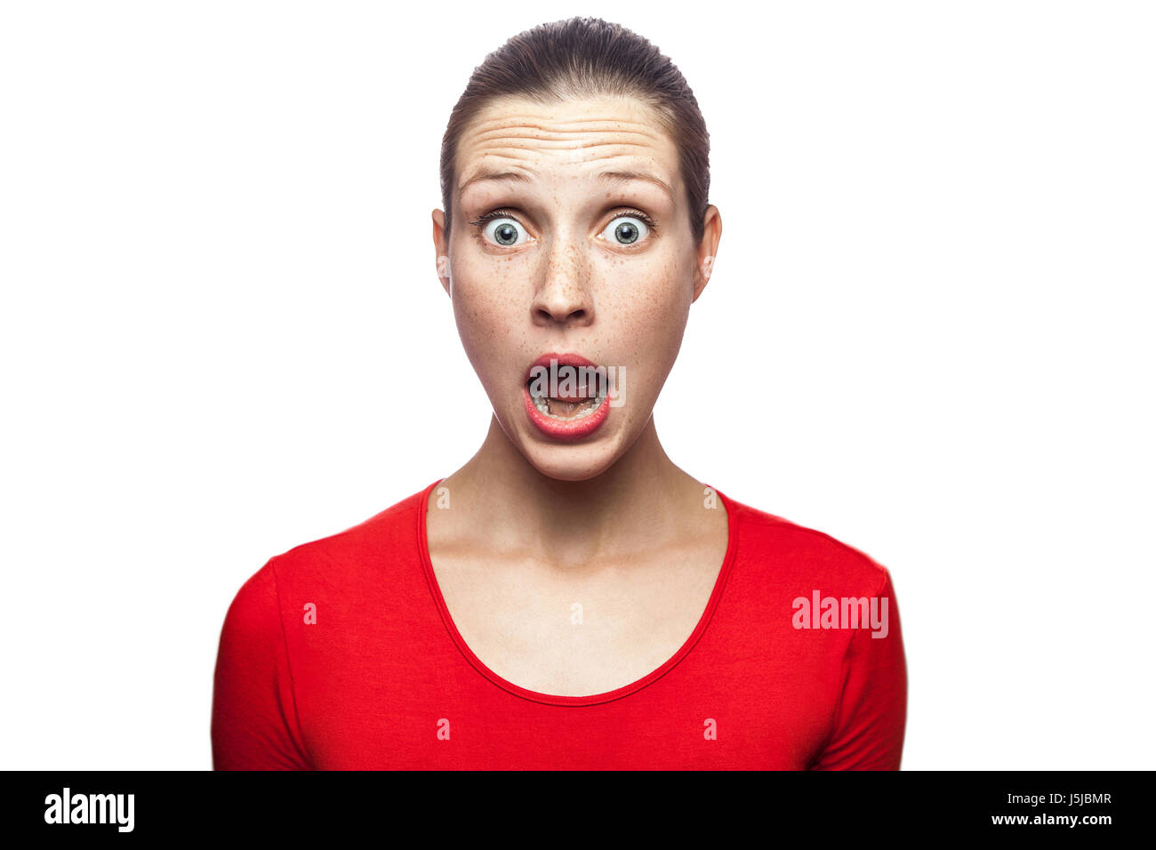 Portrait of happy surprised woman in red t-shirt with freckles. looking at camera excited with big eyes, studio shot. isolated on white background. Stock Photo