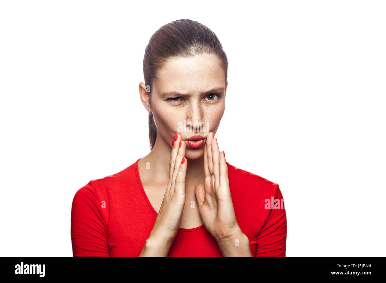 Portrait of serious woman in red t-shirt with freckles. looking at camera and telling secret, studio shot. isolated on white background. Stock Photo
