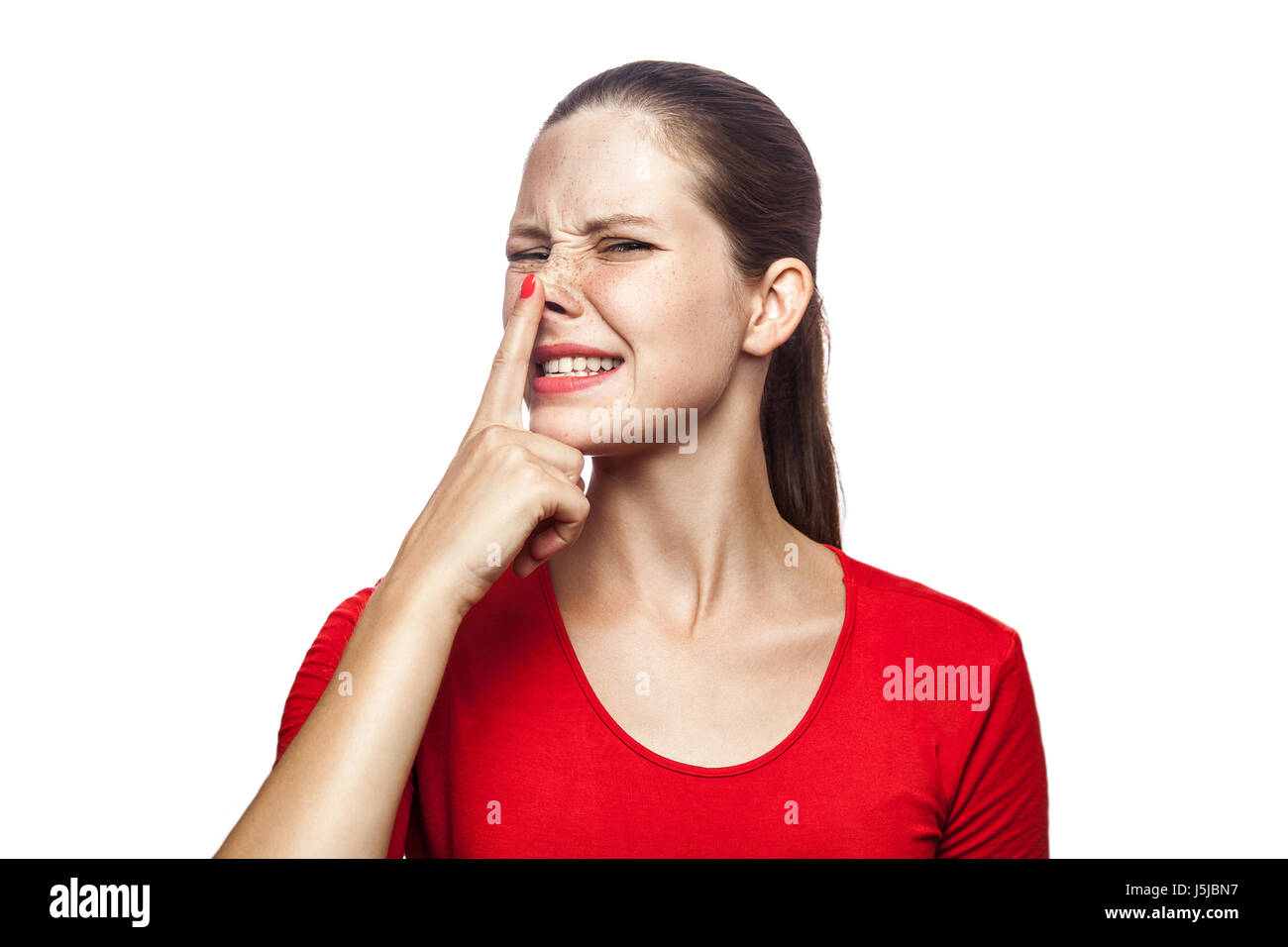 Portrait of liar woman in red t-shirt with freckles. looking up and touch her nose, studio shot. isolated on white background. Stock Photo