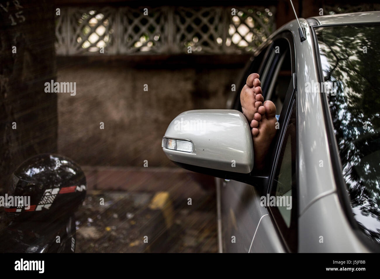 A man sleeping in his car with his feet out in Mumbai, India. Stock Photo
