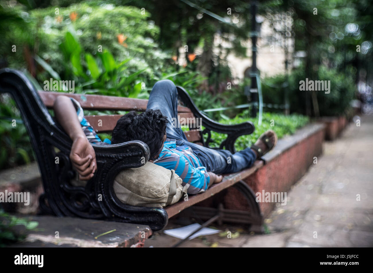 A man sleeping on a bench in a park in Mumbai during the hot summer afternoon. Stock Photo
