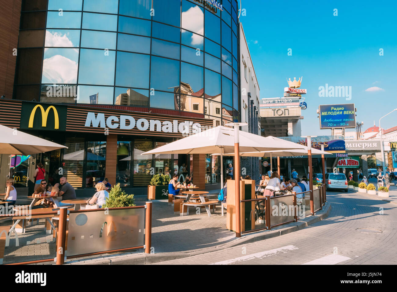 Minsk, Belarus. The Scene Of Ingestion At The Outdoor Crowded McDonald's Fast Food Restaurant On Nemiga Street In Sunny Summer Day Under Blue Sky. Stock Photo