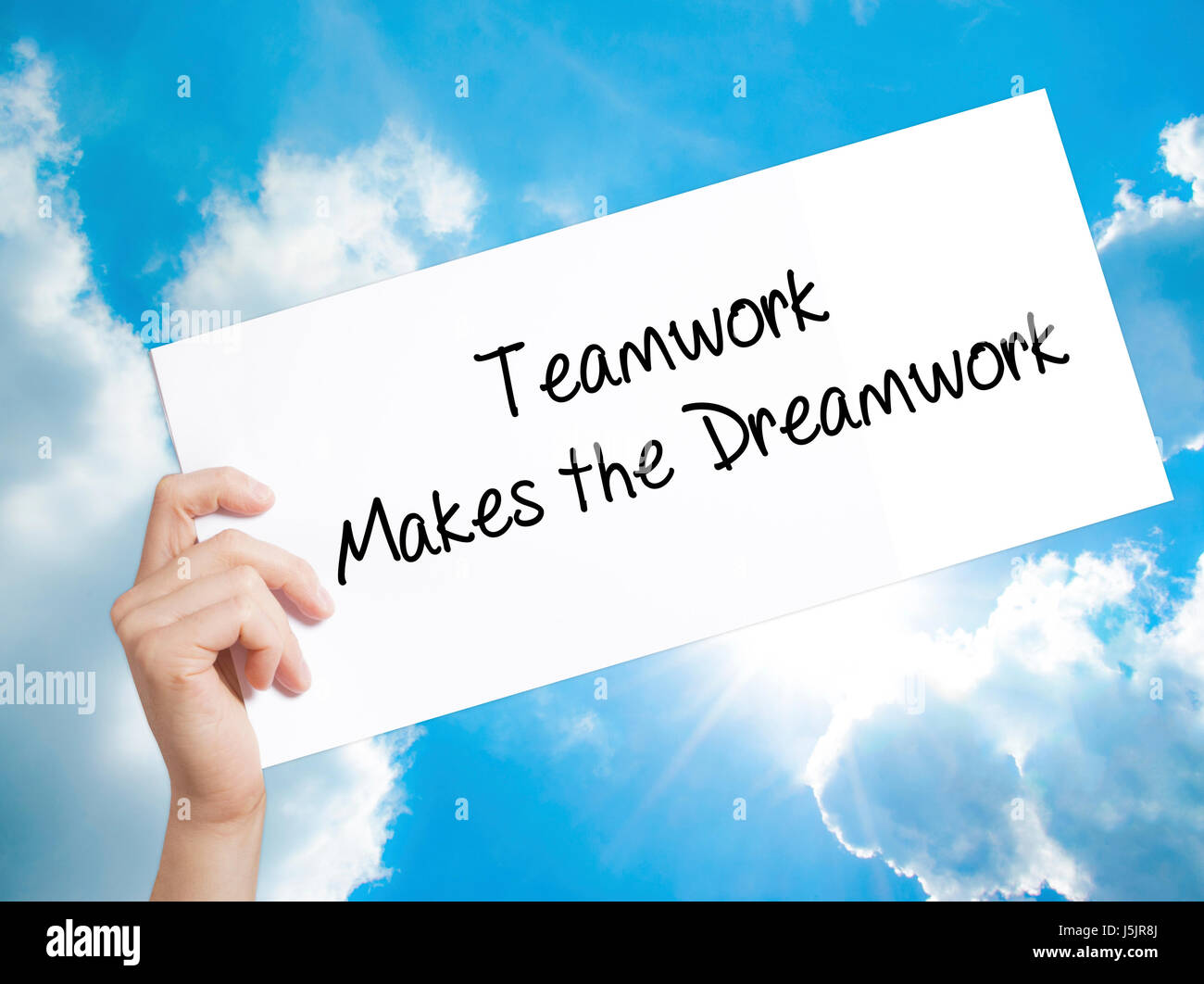 Teamwork Makes the Dreamwork Sign on white paper. Man Hand Holding Paper with text. Isolated on sky background.  Business concept. Stock Photo Stock Photo