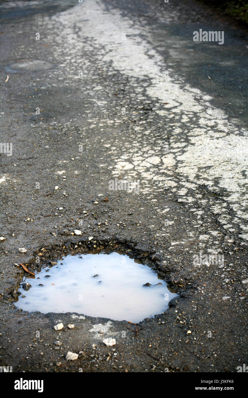 danger asphalt wet crannies hole puddle fissured cracked damaged road hole Stock Photo