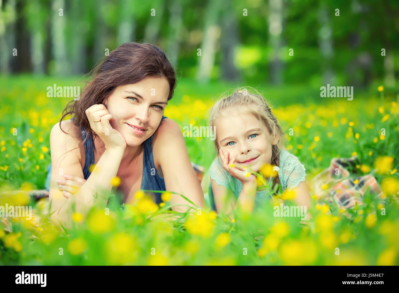 Mother and daughter lying on green summer meadow with blooming yellow flowers Stock Photo