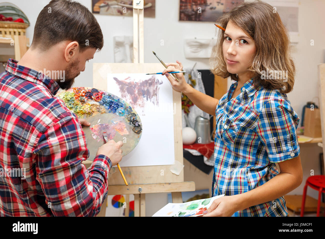 Students fool around in art school. A man and a girl draw an abstract painting with oil paints. Joint creativity. Courses of drawing for adults. Stock Photo
