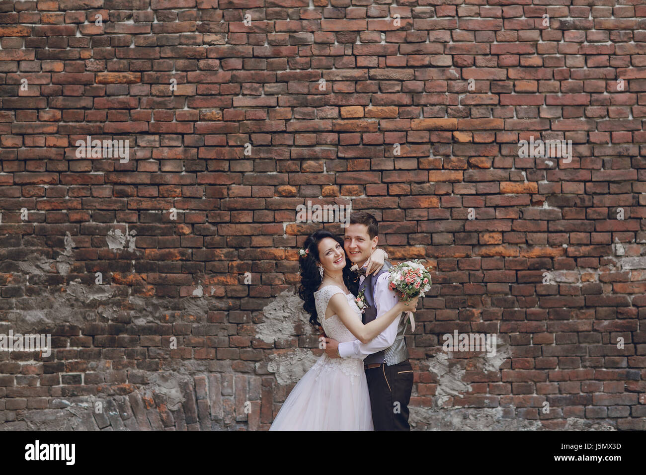 bride and groom standing at a high brick wall Stock Photo - Alamy