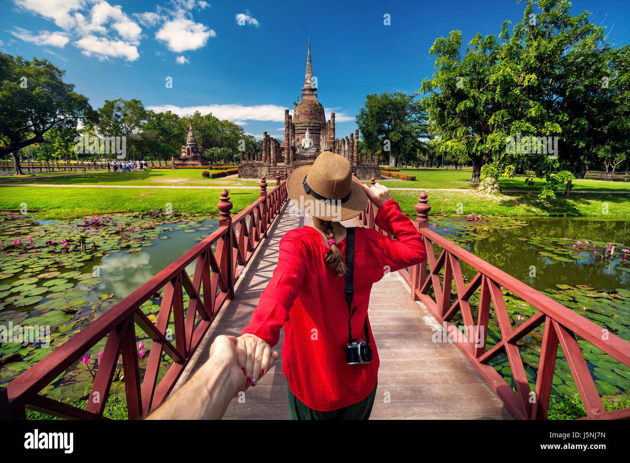 Tourist Woman in red shirt holding her husband by hand and going to ancient stupa in Sukhohai Historical Park, Thailand Stock Photo