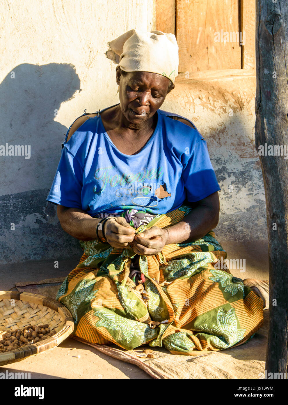 Elderly woman shelling ground nuts sitting on the khonde of her mud hut in a rural village in Malawi, Africa Stock Photo