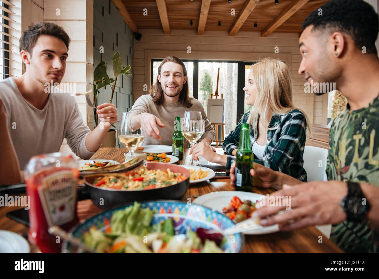 Group of happy smiling multiracial friends eating, drinking and talking at the dinner table Stock Photo